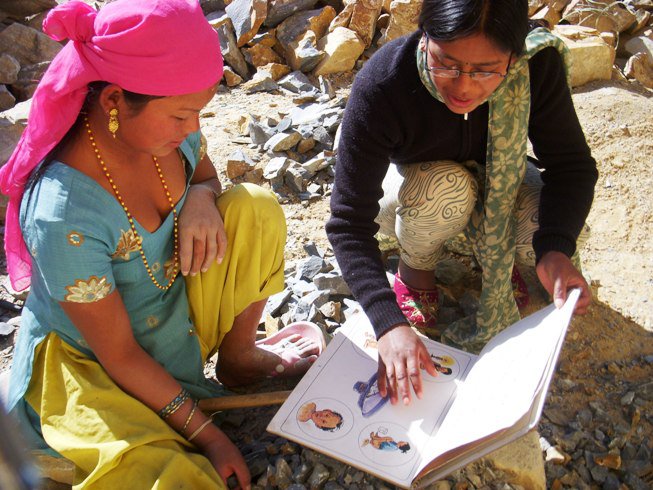 Two women sat outside on a rocky terrain discuss nutrition advice while looking through a book